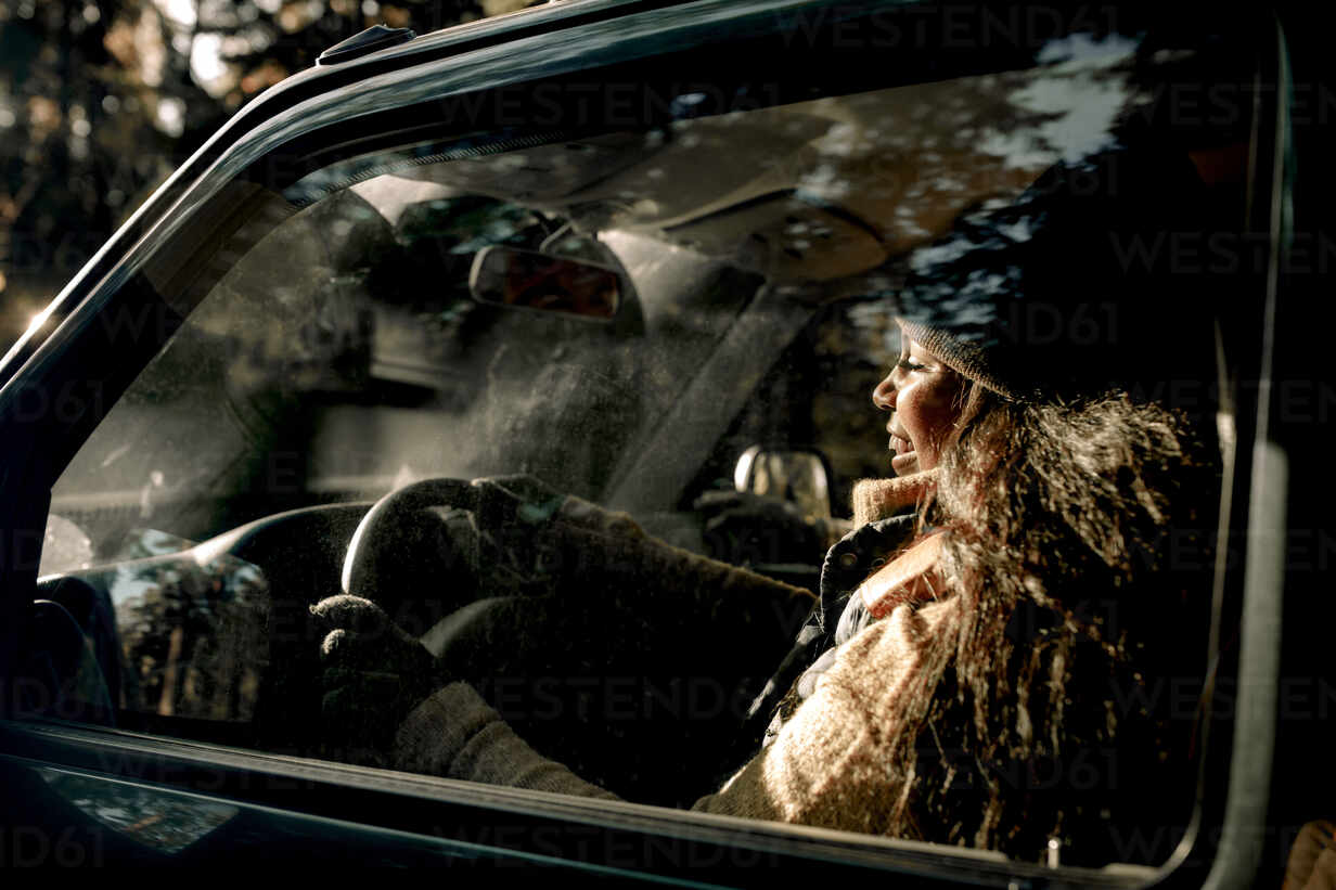 Side view of happy young woman driving off-road vehicle seen through glass stock photo