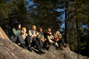 Männliche und weibliche Freunde genießen das Sonnenlicht, während sie auf einem Felsen im Wald sitzen - MASF34187