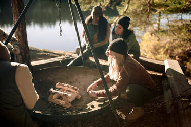 Female friends talking to each other while preparing firepit during camping - MASF34194