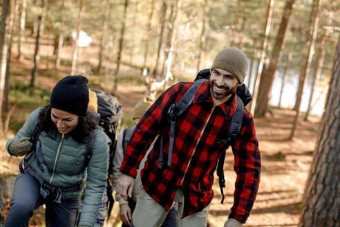 Glücklicher Mann mit kariertem Hemd beim Wandern mit einer Freundin im Wald - MASF34197