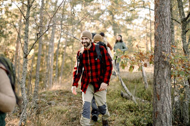 Lächelnder Mann beim Wandern mit Freunden inmitten von Bäumen im Wald - MASF34202
