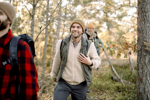 Lächelnder Mann in warmer Kleidung beim Wandern mit Freunden im Wald - MASF34203