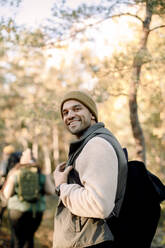 Seitenansicht eines lächelnden Mannes mit Rucksack, der im Wald steht - MASF34206