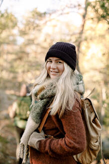 Side view of smiling young woman with backpack in forest - MASF34207