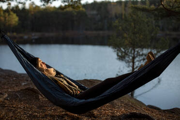 Young woman sleeping on hammock at lakeshore during sunset - MASF34213