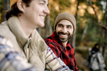 Happy man wearing plaid shirt talking to male friend during camping - MASF34222