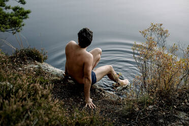 Shirtless Mann sitzt in der Nähe von See mit Beinen in Wasser getaucht - MASF34228