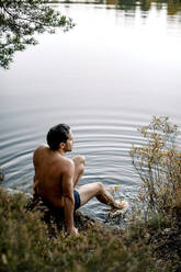 Shirtless man sitting near lake during staycation - MASF34229