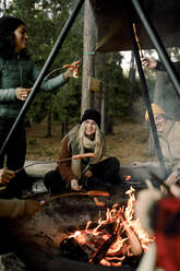 Glücklicher Mann und Freunde genießen das Essen am Lagerfeuer im Wald - MASF34232