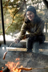 Frau brät Essen über dem Lagerfeuer beim Camping - MASF34233