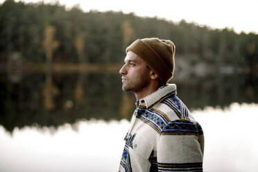 Thoughtful man in knit hat standing by lake - MASF34237