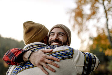 Junger Mann umarmt glücklichen männlichen Freund mit Strickmütze - MASF34243