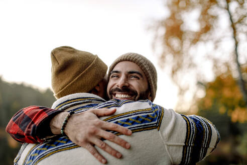 Young man embracing happy male friend wearing knit hat - MASF34243
