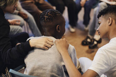 Multirassische Jungen trösten männlichen Freund in der Gruppentherapie in der Schule mit den Armen - MASF34274