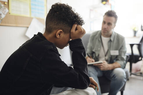 Trauriger Teenager, der bei einem männlichen Berater sitzt und im Schulbüro diskutiert - MASF34293