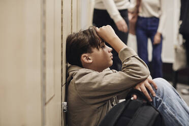 Depressiver Teenager, der an einem Spind im Schulkorridor sitzt - MASF34305