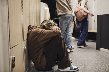 Full length of sad teenage girl sitting in school corridor - MASF34318