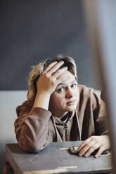 Porträt eines Teenagers, der mit dem Kopf in den Händen am Schreibtisch sitzt - MASF34325