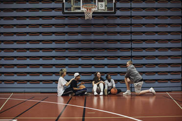 Lächelnde Jungen und Mädchen, die sich auf dem Basketballplatz in der Schule miteinander unterhalten - MASF34333