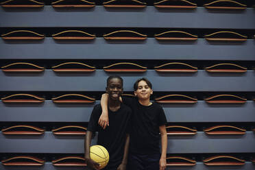 Glücklicher Jugendlicher mit Basketball, der neben einem männlichen Freund auf dem Sportplatz steht - MASF34335