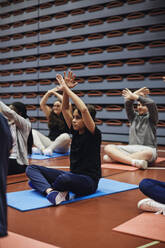 Teenager mit erhobenen Armen beim Yoga auf dem Sportplatz - MASF34351