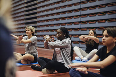 Teenage girls and boy gesturing while practicing yoga in sports court - MASF34352