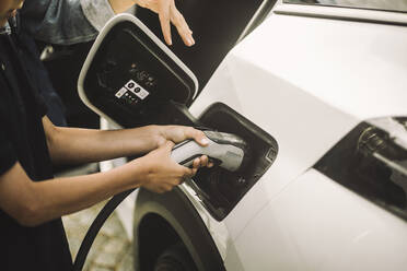 Hands of boy plugging in cable while charging electric car - MASF34382