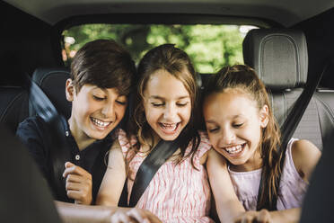 Glückliche männliche und weibliche Geschwister, die den Sicherheitsgurt tragen, während sie sich im Auto vergnügen - MASF34386
