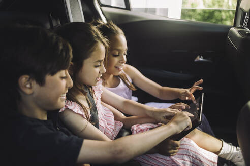 Männliche und weibliche Geschwister nutzen einen Tablet-PC während der Fahrt im Auto - MASF34389