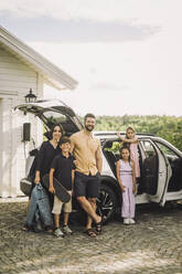 Portrait of happy family standing together outside electric car - MASF34390