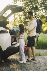 Side view of daughter and father unloading luggage from car trunk - MASF34400