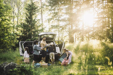 Familie entlädt Sachen aus dem Kofferraum eines Autos im Wald an einem sonnigen Tag - MASF34403