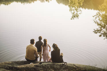 Familie schaut auf den See, während sie beim Picknick auf einem Felsen sitzt - MASF34411