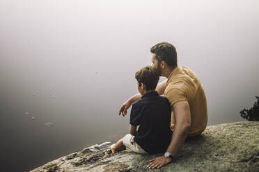 Father sitting with son on rock near lake - MASF34413