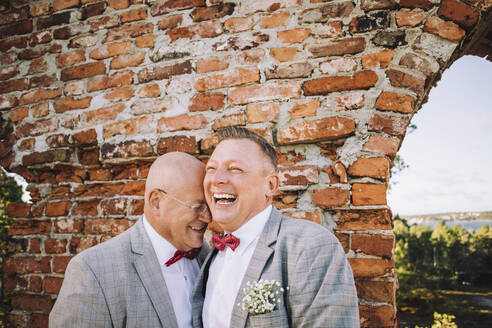 Cheerful newlywed gay couple enjoying against brick wall - MASF34421