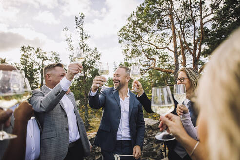 Glücklicher Bräutigam stößt mit Freunden und Familie auf der Hochzeit mit Weingläsern an - MASF34426