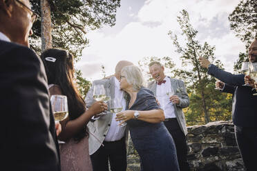 Ältere Frau umarmt Bräutigam mit Weingläsern inmitten der Hochzeitsgäste - MASF34430