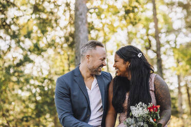 Glücklicher Bräutigam schaut auf die Braut, die einen Blumenstrauß hält - MASF34431
