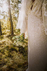 Midsection of mid adult bride wearing white wedding dress in forest - MASF34451