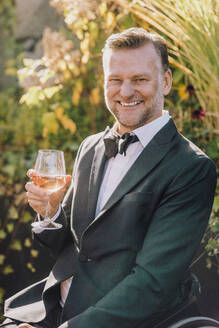 Porträt eines glücklichen Mannes im Anzug mit einem Weinglas in der Hand bei einer Hochzeit - MASF34462