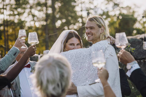 Lächelndes frisch vermähltes Paar tanzt inmitten von Familie und Freunden bei der Hochzeit - MASF34463