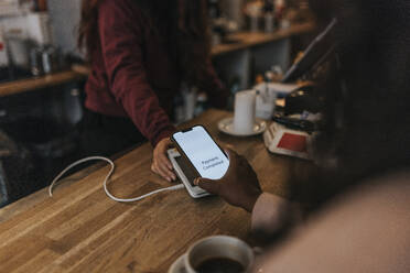 Hand einer Kundin beim kontaktlosen Bezahlen mit dem Smartphone an der Kasse eines Cafés - MASF34472