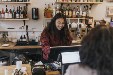 Lächelnde junge Besitzerin nimmt die Bestellung eines Kunden in einem Café entgegen - MASF34473