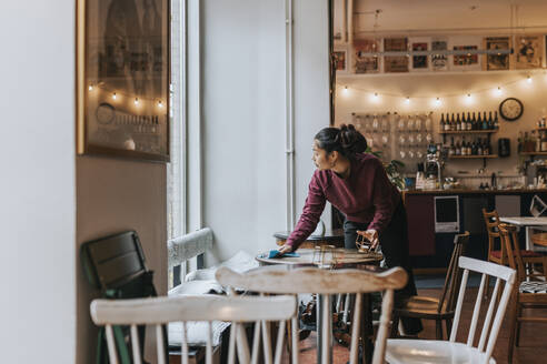 Unternehmerin reinigt Tisch mit Lappen bei der Arbeit im Café - MASF34478