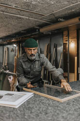Älterer Handwerker beim Einsetzen von Glas in den Rahmen an der Werkbank - MASF34506