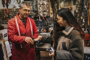 Lächelnde junge Kundin beim kontaktlosen Bezahlen mit Kreditkarte in einer Werkstatt - MASF34538