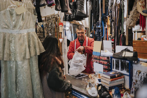 Rückansicht einer Kundin im Gespräch mit einem Ladenbesitzer, der eine Plastiktüte hält - MASF34540