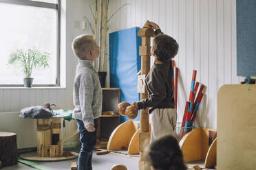 Boy stacking toy blocks while male friend looking at him in day care center - MASF34550