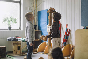 Junge stapelt Spielzeugblöcke, während ein männlicher Freund ihn in der Kindertagesstätte beobachtet - MASF34550