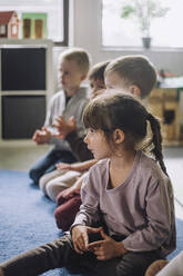 Gemischtrassige Kinder sitzen auf einem Teppich im Kindergarten - MASF34552